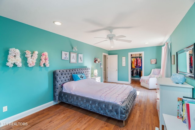 bedroom with a spacious closet, a closet, ceiling fan, and hardwood / wood-style flooring