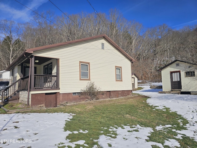 view of snowy exterior featuring a porch, a yard, and a storage shed