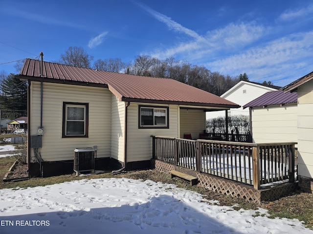 snow covered back of property with cooling unit and a deck