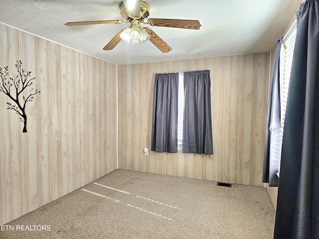 empty room with ceiling fan, wooden walls, carpet floors, and a textured ceiling