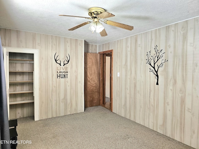 unfurnished room featuring carpet floors, a textured ceiling, wooden walls, and ceiling fan