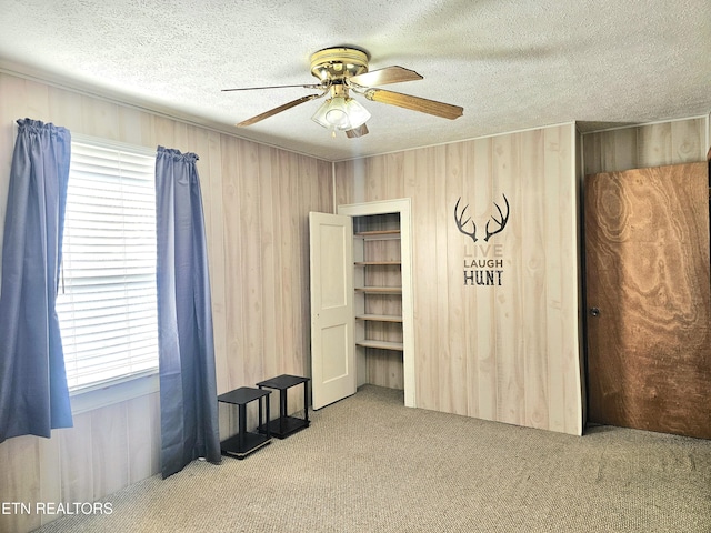 carpeted bedroom with multiple windows, wooden walls, a textured ceiling, and ceiling fan