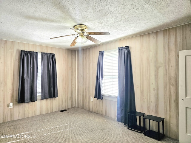 carpeted empty room with a textured ceiling, ceiling fan, and wood walls