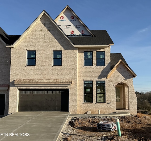 view of front of home featuring a garage, driveway, brick siding, and roof with shingles