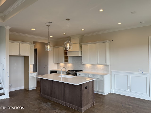 kitchen featuring decorative backsplash, stainless steel gas range oven, a center island with sink, a sink, and light countertops