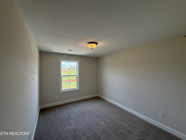 spare room featuring baseboards, dark carpet, a textured ceiling, and visible vents