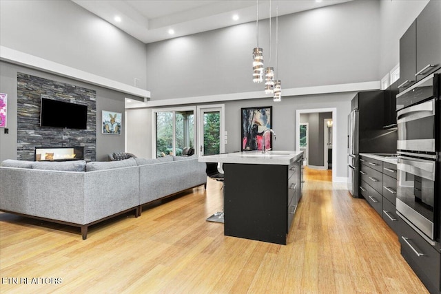 living room featuring a high ceiling, a stone fireplace, sink, and light hardwood / wood-style floors