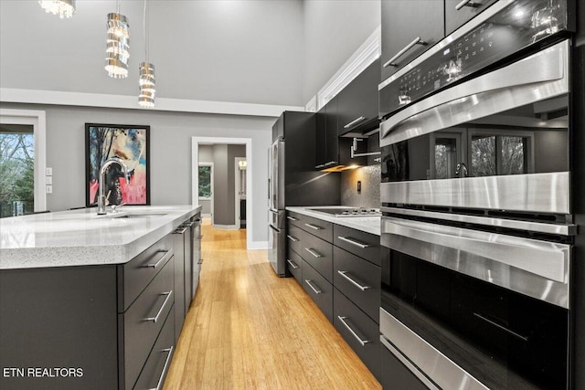 kitchen featuring sink, light hardwood / wood-style flooring, an island with sink, pendant lighting, and stainless steel double oven