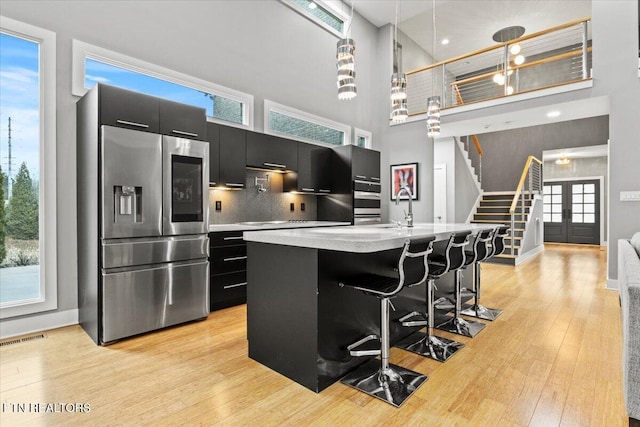 kitchen featuring a breakfast bar, hanging light fixtures, stainless steel appliances, a center island with sink, and light wood-type flooring