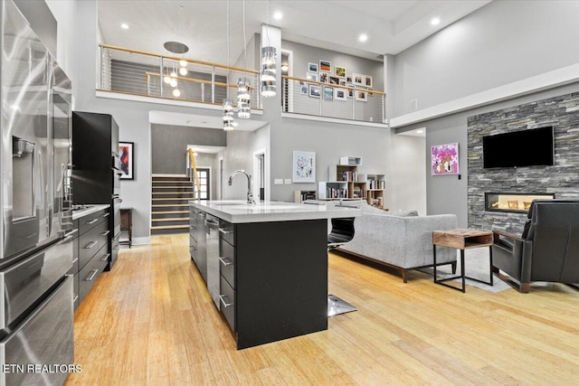 kitchen with sink, stainless steel fridge, a center island with sink, decorative light fixtures, and light wood-type flooring