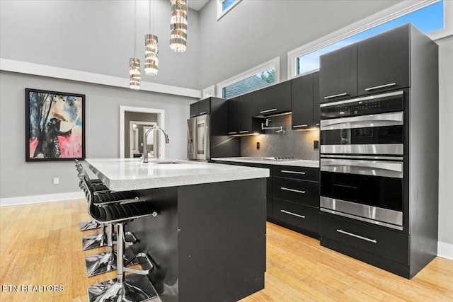 kitchen with sink, appliances with stainless steel finishes, a kitchen island with sink, a kitchen breakfast bar, and decorative light fixtures