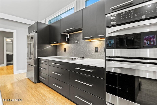 kitchen with stainless steel double oven, cooktop, decorative backsplash, and light hardwood / wood-style flooring