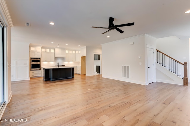 unfurnished living room with crown molding, sink, ceiling fan, and light hardwood / wood-style flooring