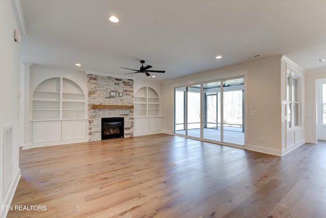 unfurnished living room featuring built in shelves, crown molding, light hardwood / wood-style flooring, ceiling fan, and a fireplace