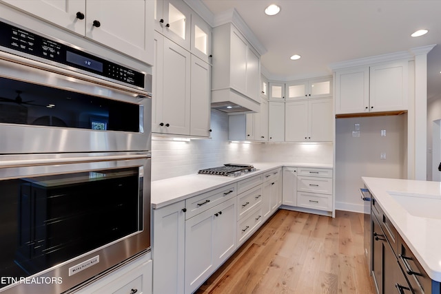 kitchen featuring appliances with stainless steel finishes, light wood-type flooring, decorative backsplash, and white cabinets