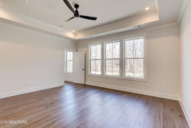 empty room featuring hardwood / wood-style flooring, ceiling fan, ornamental molding, and a tray ceiling