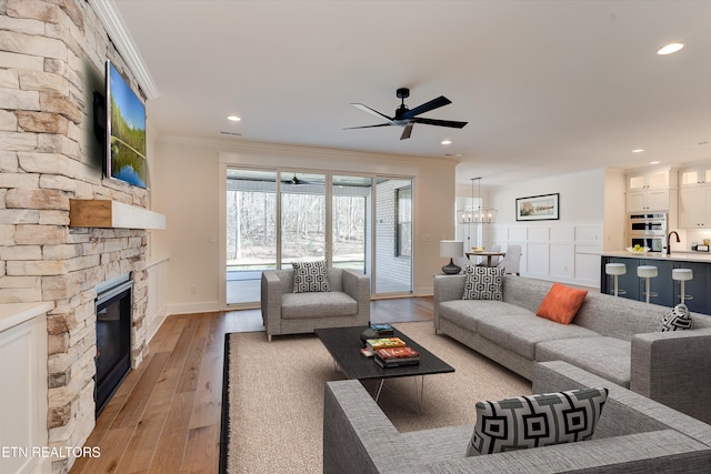 living room with sink, crown molding, light wood-type flooring, a fireplace, and ceiling fan with notable chandelier