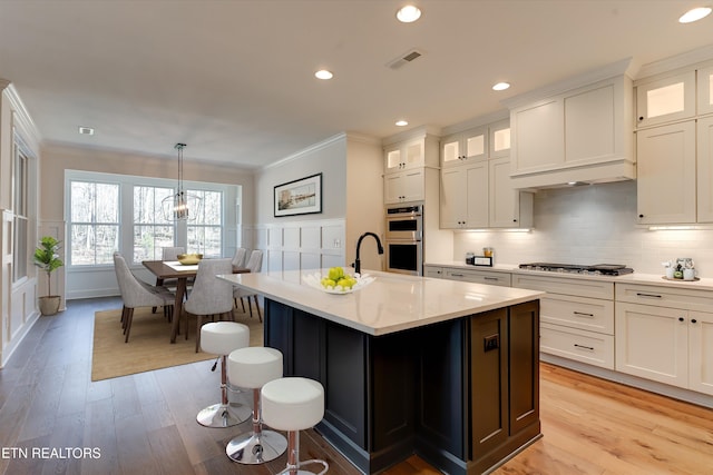 kitchen with pendant lighting, appliances with stainless steel finishes, an island with sink, and white cabinets