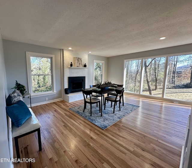 dining space with a brick fireplace, light hardwood / wood-style floors, and a textured ceiling