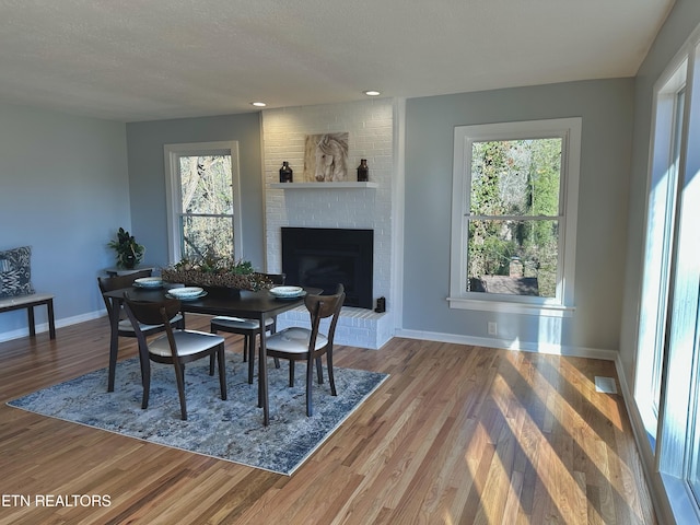 dining area with hardwood / wood-style flooring, a fireplace, a textured ceiling, and a wealth of natural light