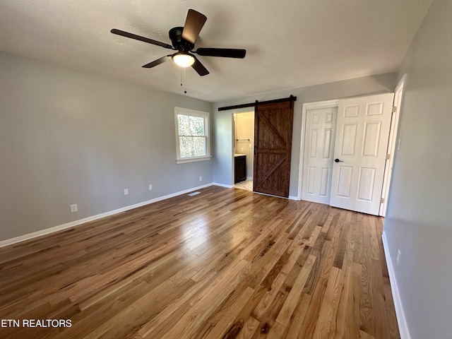 unfurnished bedroom featuring hardwood / wood-style flooring, ensuite bath, a barn door, and a closet