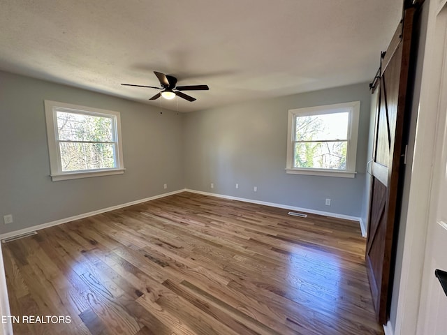 spare room featuring hardwood / wood-style flooring, ceiling fan, a healthy amount of sunlight, and a barn door