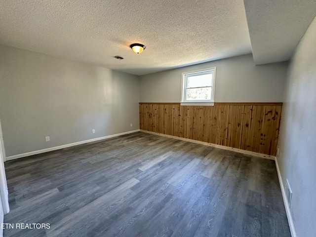 empty room featuring dark hardwood / wood-style flooring, wooden walls, and a textured ceiling