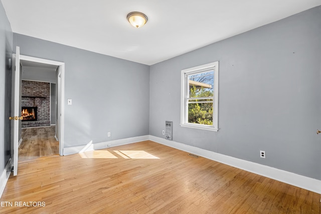 unfurnished room with hardwood / wood-style flooring and a brick fireplace