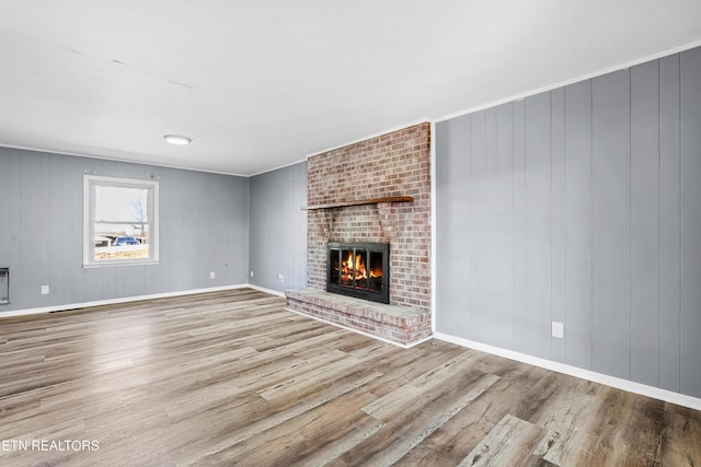 unfurnished living room with a brick fireplace, light hardwood / wood-style floors, and wood walls