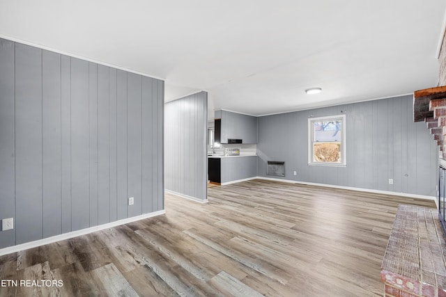 unfurnished living room with light hardwood / wood-style floors, a brick fireplace, and wood walls