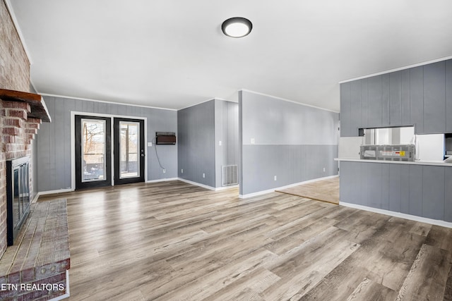 unfurnished living room featuring a fireplace, ornamental molding, an AC wall unit, and light wood-type flooring