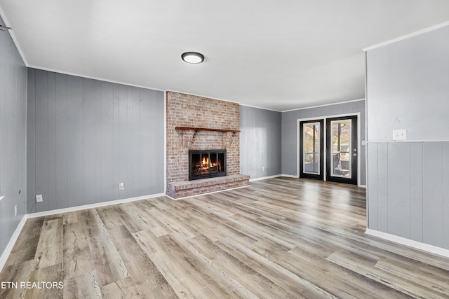 unfurnished living room with crown molding, a fireplace, wood walls, and light wood-type flooring