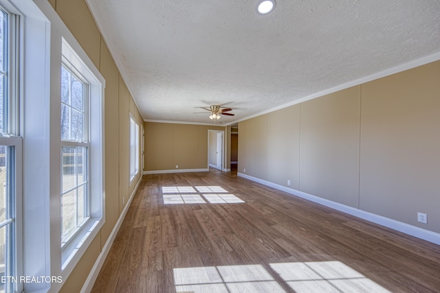 empty room with wood-type flooring, a wealth of natural light, a textured ceiling, and crown molding