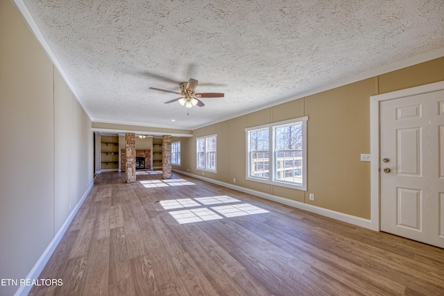 unfurnished living room with ceiling fan, a textured ceiling, a fireplace, and light wood-type flooring