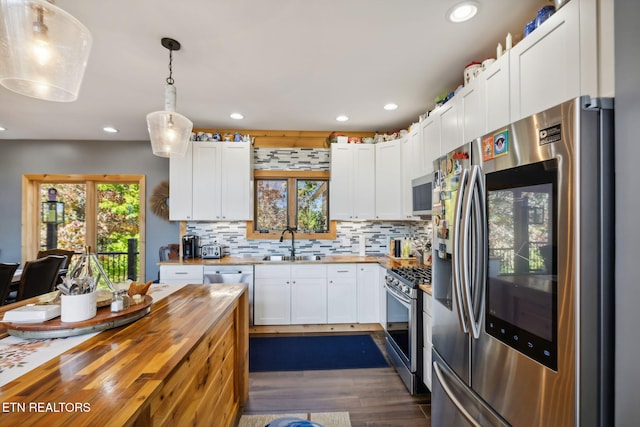 kitchen with pendant lighting, butcher block countertops, sink, white cabinets, and stainless steel appliances