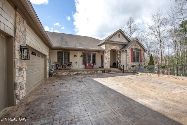 view of front of home featuring decorative driveway, a porch, fence, a garage, and stone siding