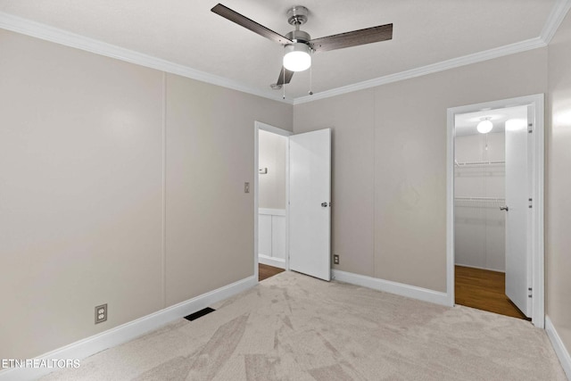 unfurnished bedroom featuring a walk in closet, ornamental molding, light colored carpet, and ceiling fan