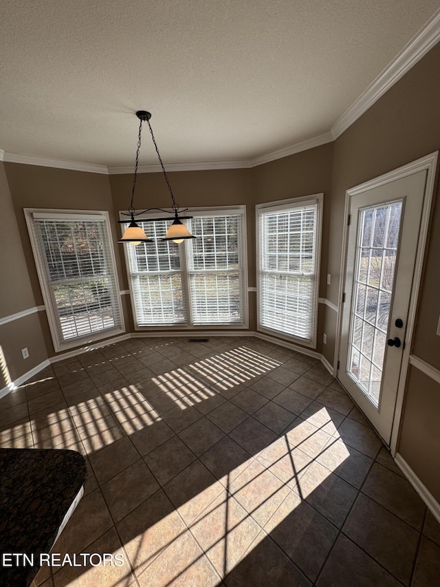 unfurnished dining area with a textured ceiling, ornamental molding, and dark tile patterned floors