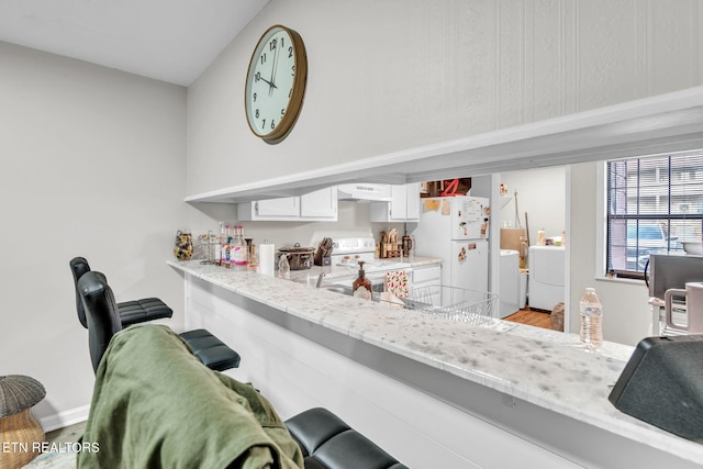 kitchen with white cabinets, white appliances, light stone counters, independent washer and dryer, and light wood-type flooring