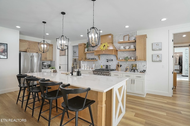 kitchen with range, a kitchen island with sink, premium range hood, white cabinets, and a kitchen bar