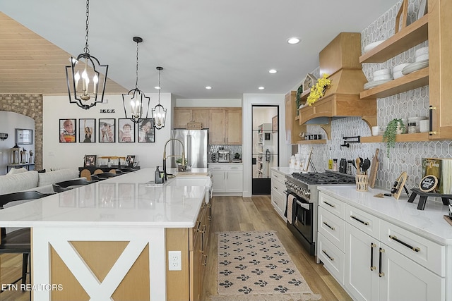 kitchen with a breakfast bar, high quality appliances, white cabinets, backsplash, and a center island with sink