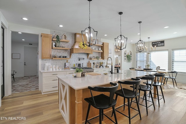 kitchen with premium range hood, an island with sink, white cabinets, a kitchen breakfast bar, and light hardwood / wood-style flooring