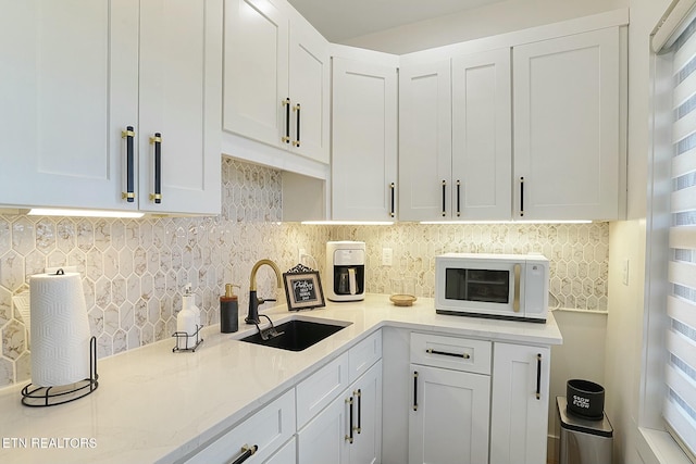 kitchen featuring white cabinetry, light stone countertops, sink, and backsplash