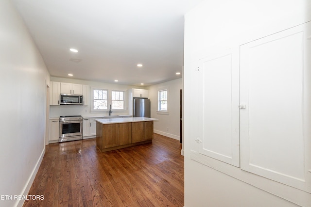 kitchen with appliances with stainless steel finishes, dark wood-type flooring, a center island, light countertops, and white cabinetry