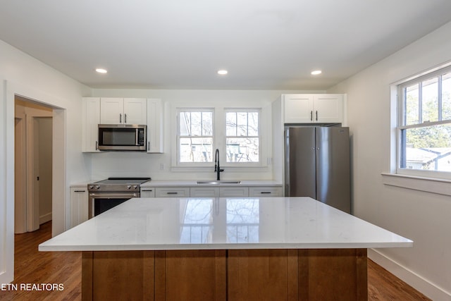 kitchen featuring stainless steel appliances, a kitchen island, a sink, white cabinets, and light stone countertops