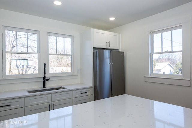 kitchen with plenty of natural light, freestanding refrigerator, white cabinetry, and a sink