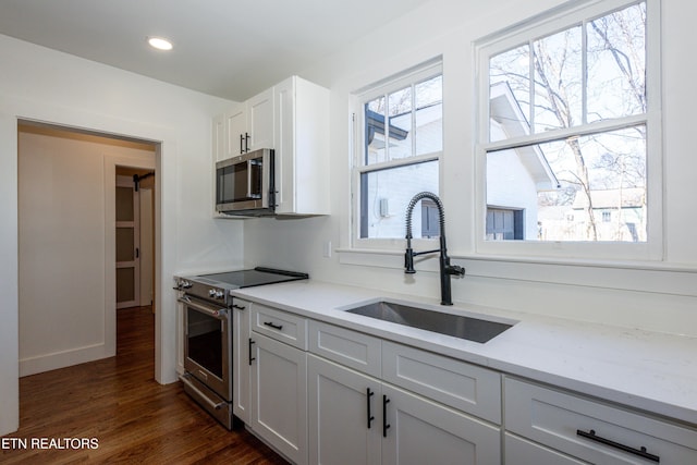 kitchen featuring light stone counters, a sink, white cabinets, appliances with stainless steel finishes, and dark wood-style floors