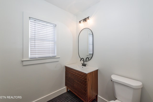 half bathroom with baseboards, vanity, and toilet