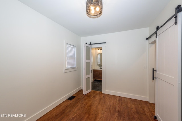 unfurnished bedroom with a barn door, dark wood finished floors, visible vents, and baseboards