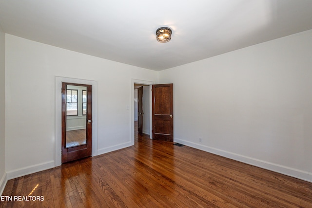 spare room featuring dark wood-type flooring, visible vents, and baseboards